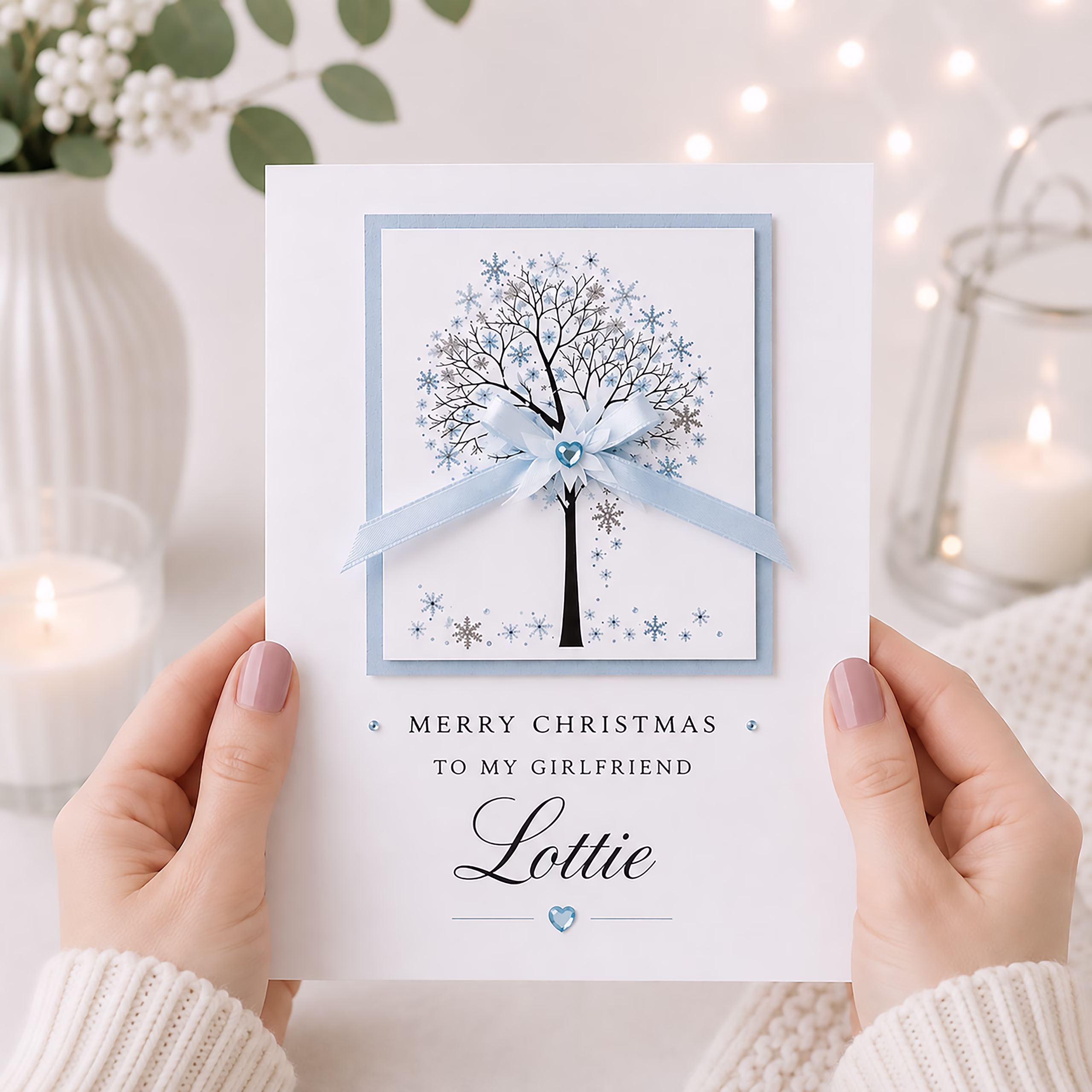Elegant white Christmas card displayed in a light festive setting, with a blue winter tree design, ribbon bow and crystal-style embellishments.