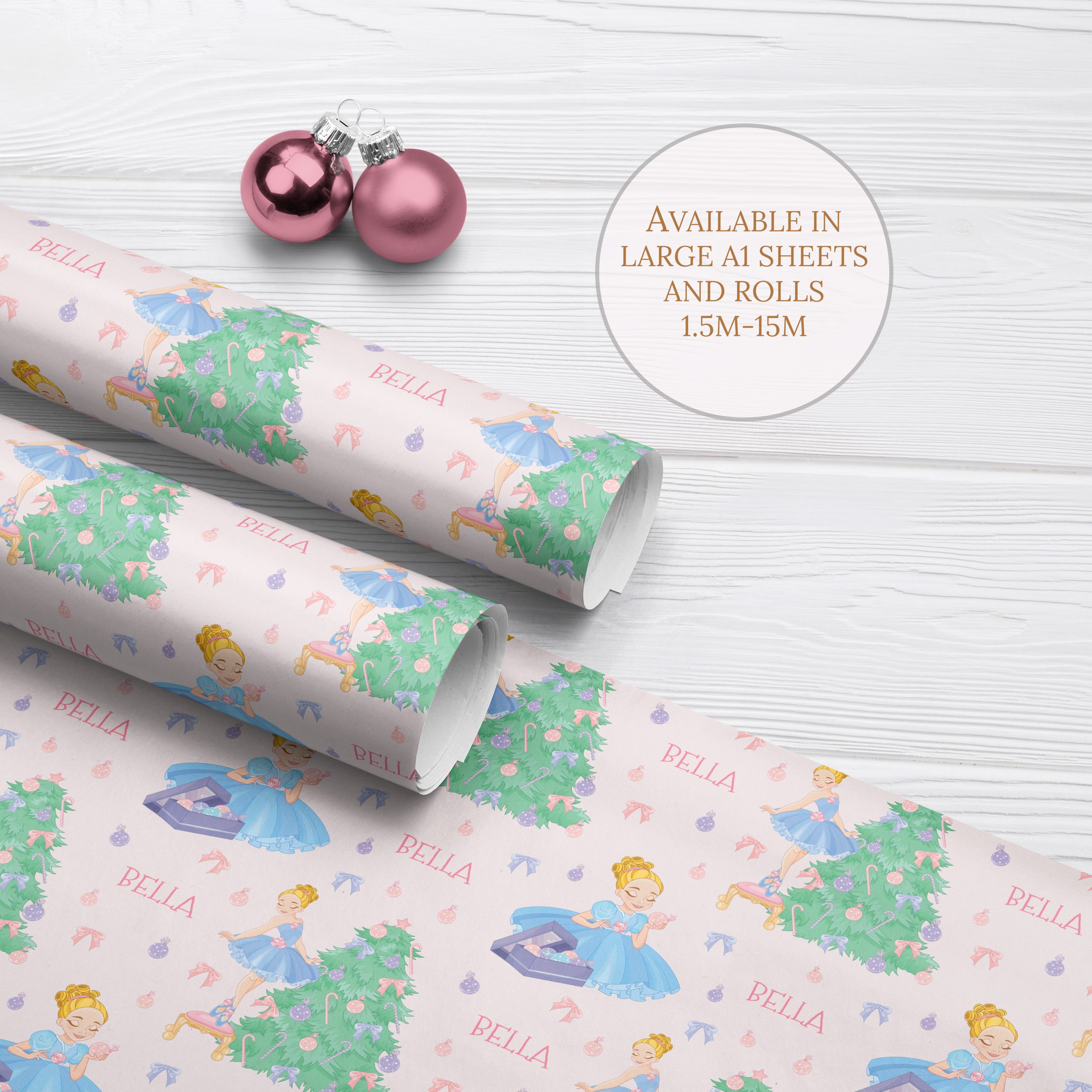 Personalised Ballerina Princess Wrapping Paper, two rolls and one sheet on a white wood background with two pink christmas baubles. Christmas wrapping paper features a ballerina princess in a blue dress decorating a large christmas tree with baubles.