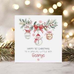 baby's 1st personalised christmas card featuring a festive wreath with a snowman, teddy and clear christmas bauble hanging from it. The baby's name appears underneath.