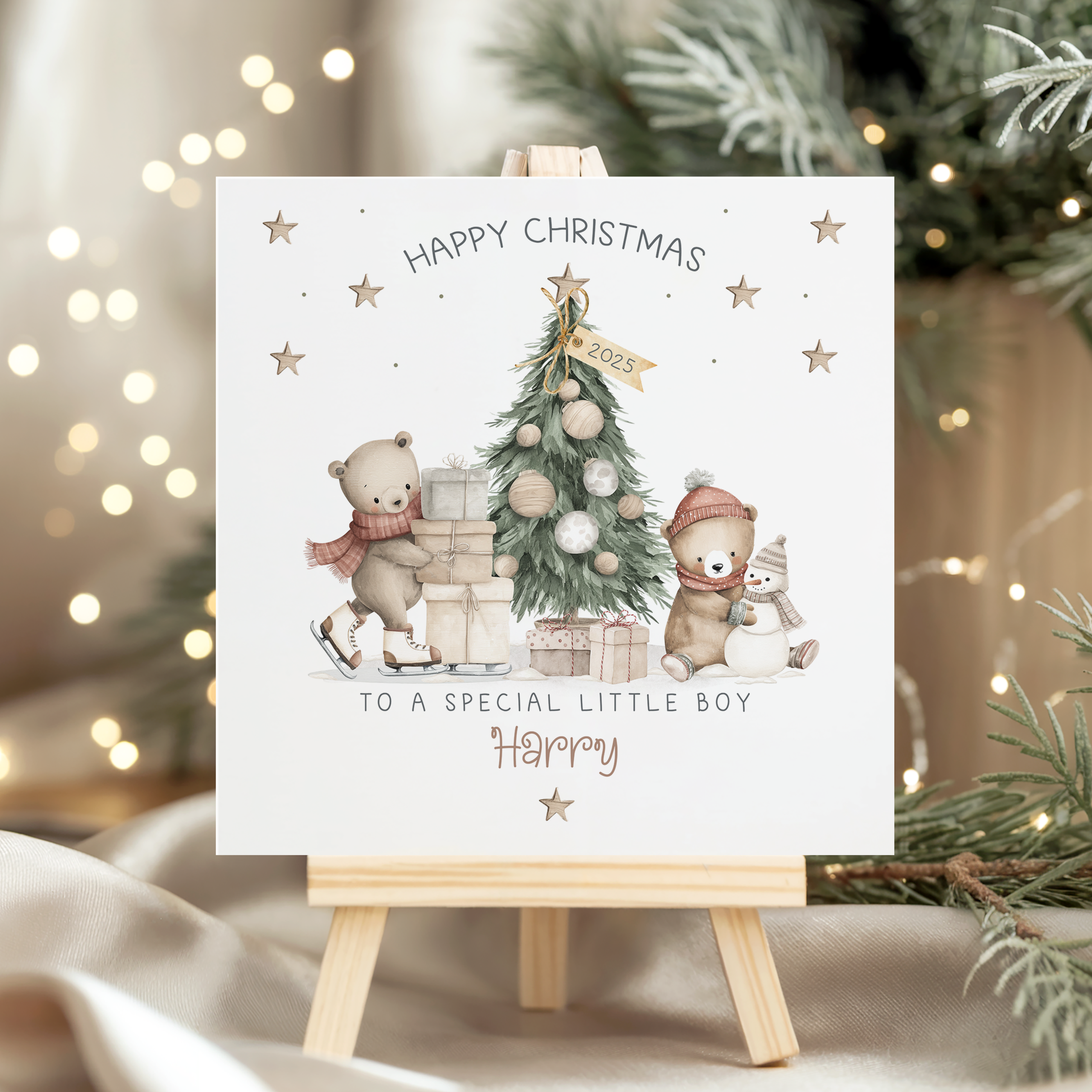 Personalised Teddy Bear Christmas card for children. Featuring a christmas tree with a skating bear with a pile of gifts and a seated bear making a snowman. Personalised at the bottom with the childs name in an ornate brown christmassy font.