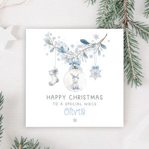 Girls personalised bunny rabbit christmas card. Featuring a blue floral wreath with christmas baubles hanging from it, a star, a christmas stocking and a bauble with a cute bunny rabbit. The card is personalised at the bottom with a name in blue ornate christmassy font.