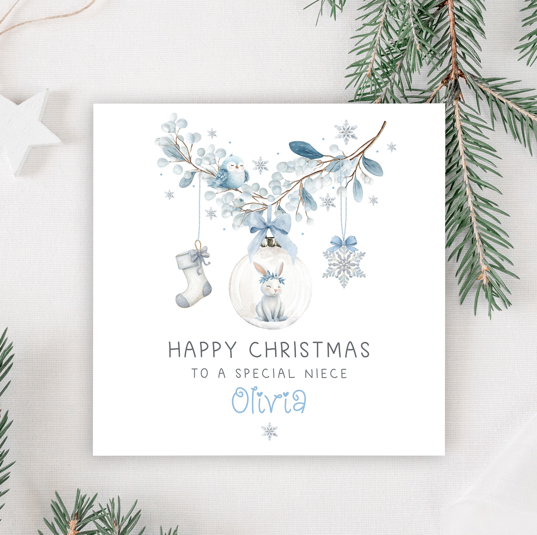 Girls personalised bunny rabbit christmas card. Featuring a blue floral wreath with christmas baubles hanging from it, a star, a christmas stocking and a bauble with a cute bunny rabbit. The card is personalised at the bottom with a name in blue ornate christmassy font.